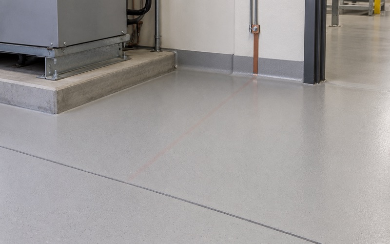 A smooth gray floor with coved edges beneath industrial equipment.